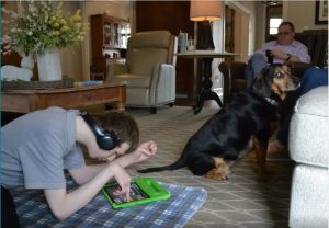 Patrick Gunnells, 23, left, watches videos on his iPad in the living room at his Tupelo home on Mar. 9, 2023 while his dad, Jamie Gunnells, takes a break from running the family's independent pharmacy. For several years, Patrick Gunnells, who has severe autism, has been without a daily caregiver, meaning his parents work around-the-clock to meet all of his needs. Credit: Anna Wolfe