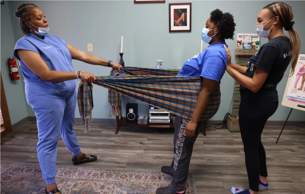 Community Health Director Yolanda Davis, left, shows Kayla Davis, center, Skyler Jackson how to relieve back pain during a childbirth prep class at Sisters in Birth in Jackson, Miss., Saturday, June 4, 2022. The class teaches husbands and partners to be doulas. Credit: Eric Shelton/Mississippi Today
