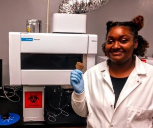 Takaye Farmer, a senior chemistry major at MC, holds a pottery shard that will be crushed, prepared, and fed into the state-of-the-art ICP-OES instrument for analysis.