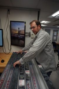 Dr. Jeremy Deans prepares halved cores of serpentinized peridotite for analysis in the core lab of the scientific drilling ship JOIDES Resolution. Photo credit: Lesley Anderson