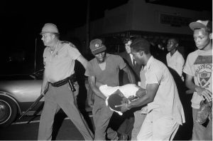 Benjamin Brown being carried away after he was shot by the police in Jackson, Miss. in May 1967. At left, Lloyd Jones, a state trooper who would later be implicated in the shooting, leads the group down a street. Credit: Bettmann, via Getty Images