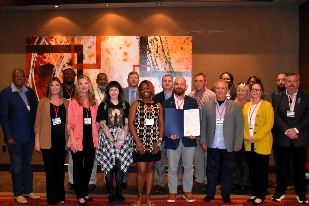 DMH staff members and veterans gathered during a break at the annual Mental Health/Intellectual and Developmental Disabilities Conference to recognize Gov. Reeves' proclamation of Veterans' Suicide Awareness Week. Pictured are (front row, L to R) Jessie Killingsworth, DMH Chief of Staff Katie Storr, DMH Executive Director Wendy Bailey, Laura Gottschalck, Katherine Johnson, DMH Medical Director Dr. Thomas Recore, Dr. Jesse Higdon, Nicole Sanders, Danny Blanton, (back row, L to R) Daniel Myers, Willis Garrison, DMH Deputy Executive Director for Behavioral Health Services Jake Hutchins, DMH Deputy Executive Director for IDD Services Craig Kittrell, Rickey Grimes, Courtney Littleton, Elaine Sendelweck, Ja'Quila Newsome, and Jeremy Reid.