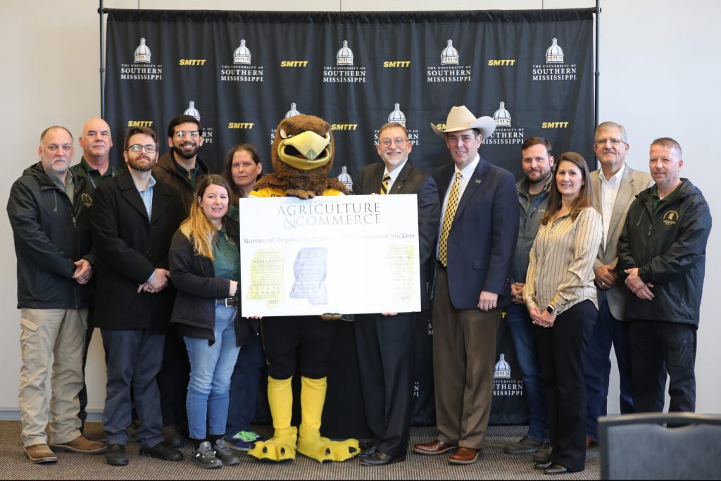 Today, Ag Commissioner Andy Gipson announced a promotional partnership between MDAC and USM. Pictured L-R: Charles Champagne, Weights and Measures Inspector; Dan Parks, Weights and Measures Inspector; Henri Fuselier, Consumer Protection Division Director; Jordan Proctor, Petroleum Inspector; Candis Hillman, Consumer Protection Inspector; Sarah Broome, Consumer Protection Inspector; Seymour the USM Golden Eagle Mascot; Dr. Lance Nail, USM Provost and Senior Vice President for Academic Affairs; Commissioner Andy Gipson; Clay Hammons, Petroleum Division Director; Jennifer Thompson, Bureau of Regulatory Services Director; Brent Bowman, Weights and Measures Division Director; and Scotty Deare, Petroleum Inspector.