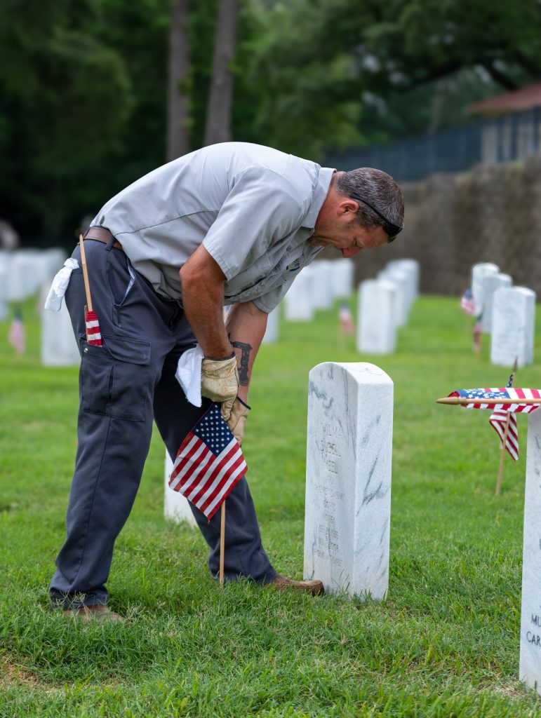 Anthony Cupit, cemetery caretaker at Natchez National Cemetery, places a flag on the gravesite of a U.S. military veteran in 2024. Photo courtesy of Caleb Q. Ray of the Natchez National Cemetery