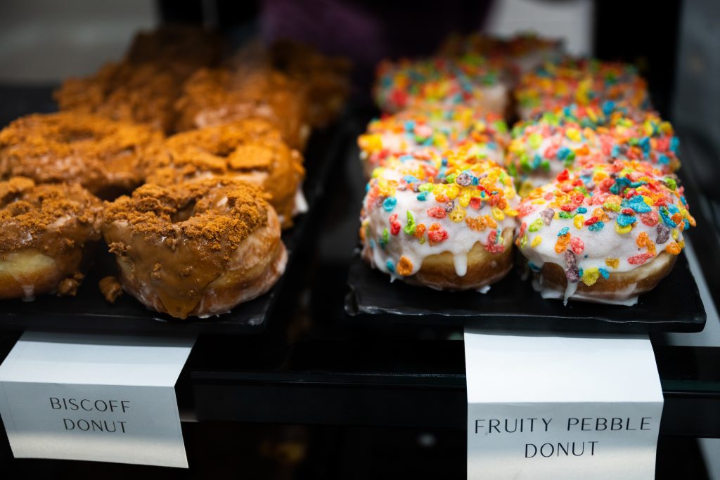 A variety of donuts are sold in State Fountain Bakery and are part of a menu that rotates weekly. Here, Biscoff and Fruity Pebbles donuts wait for a hungry customer to spot them in the display case. (Photo by Grace Cockrell)