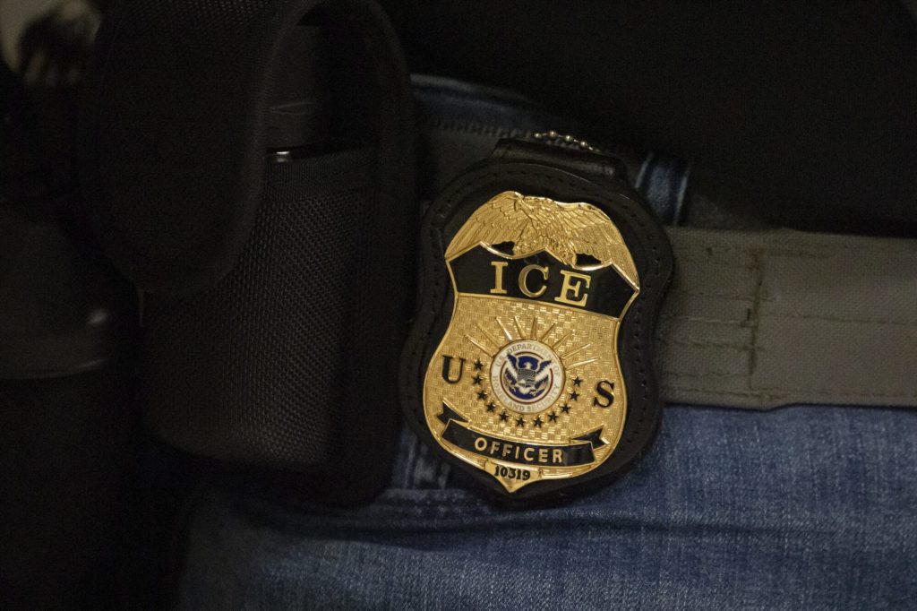 A federal agent wears a badge of Immigration and Customs Enforcement while standing outside an immigration courtroom at the Jacob K. Javits Federal Building in New York, Tuesday, June 10, 2025. (AP Photo/Yuki Iwamura)