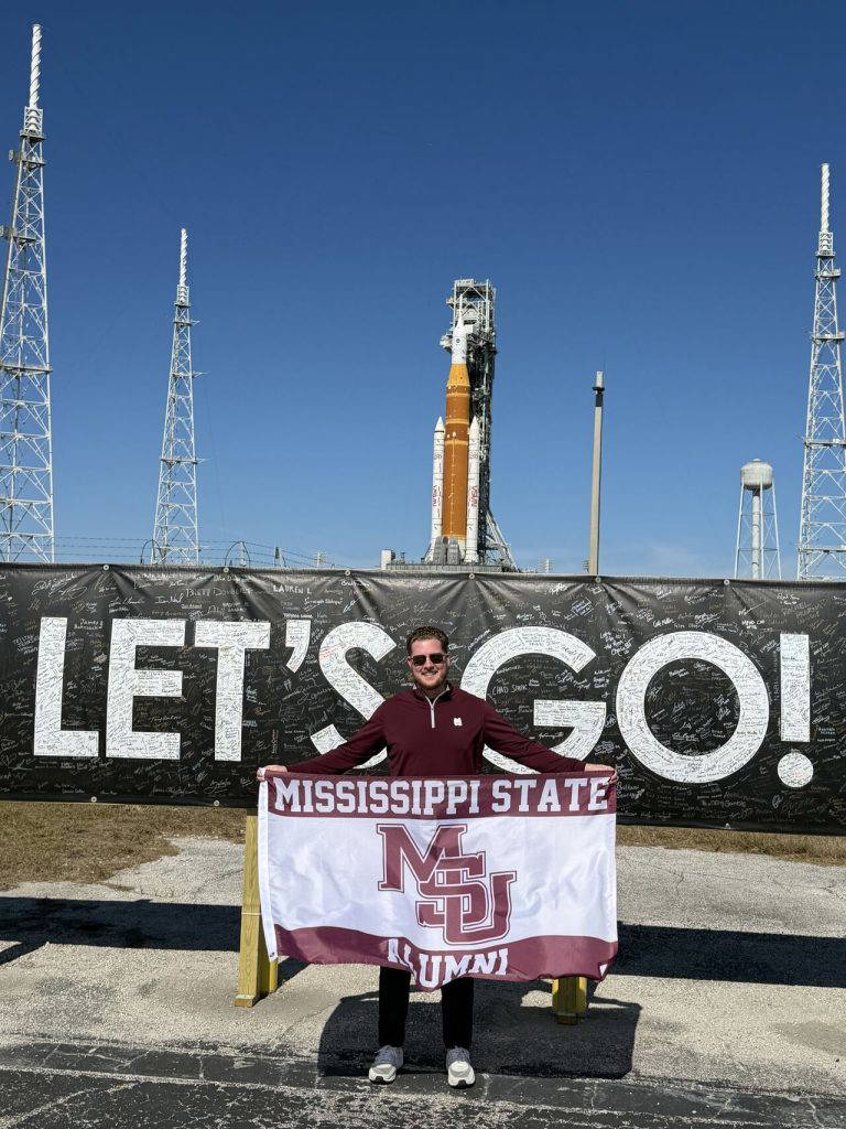 Parker Glass holds an MSU alumni flag in front of the NASA launch pad. (Photo submitted)
