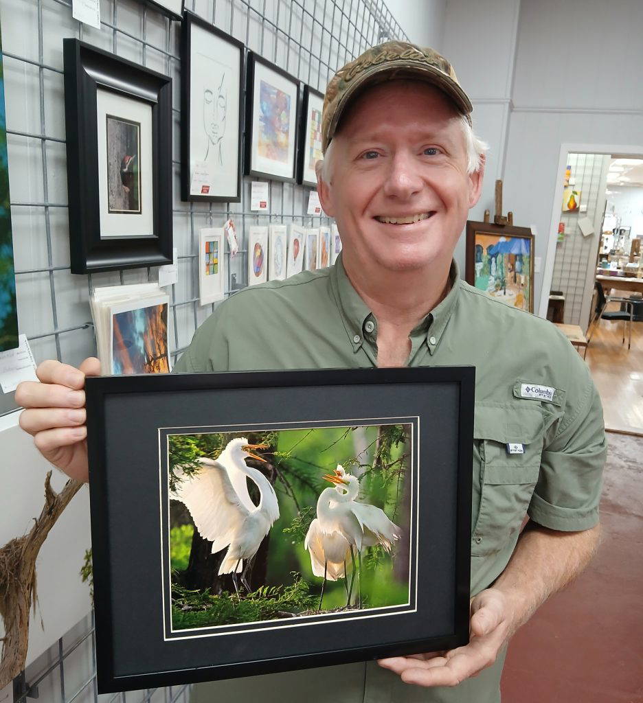 Dr. Robert Field Jr., ArtsNatchez’s Artist of the Month for August, displays one of his featured wildlife photographs depicting a great egret returning to the nest as her chicks await. The image is among several of Field’s photographs on display at the ArtsNatchez Gallery in downtown Natchez. Photo by Roscoe Barnes III.
