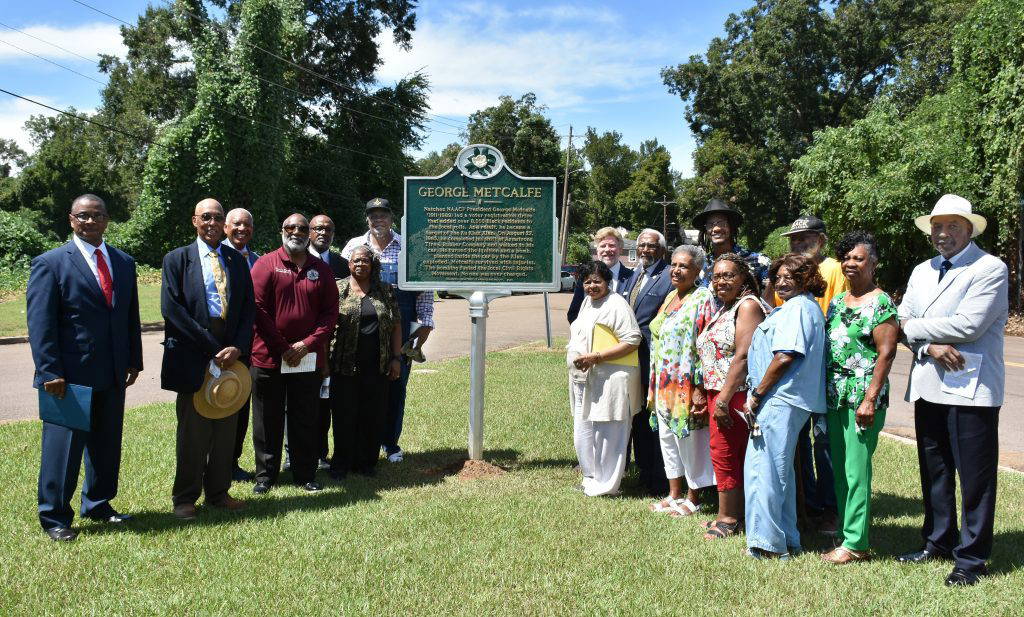 Community members pose beside a Mississippi historical marker honoring civil rights leader George Metcalfe at the site of the August 27, 1965, bombing that nearly claimed his life. The marker, approved by the Mississippi Department of Archives and History, stands near the former Armstrong Tire and Rubber Company in Natchez.Photo by Albert L. Jones